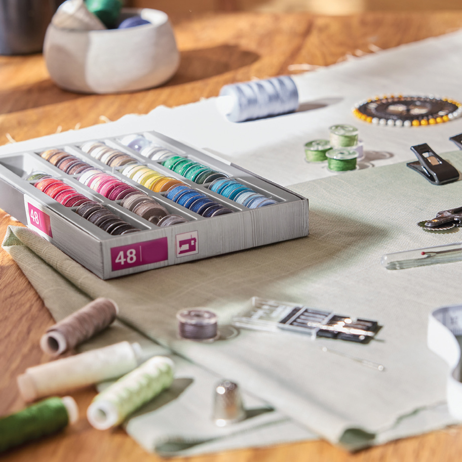 Kutija sa 48 kalema konca za šivenje u raznim bojama, sa priborom za šivenje na stolu.