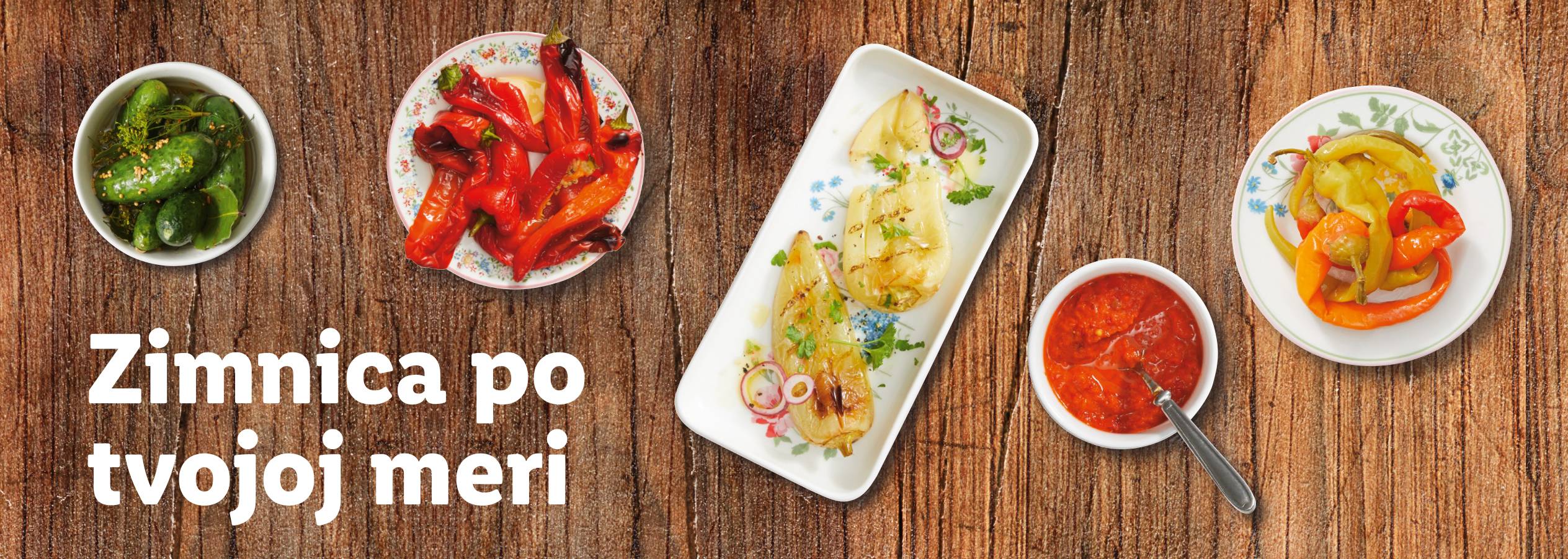 Raznovrsna zimnica na drvenoj pozadini: kiseli krastavci, pečene paprike, ajvar.
